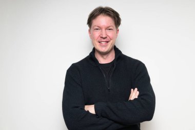 İskandinav orta yaşlı adam beyaz stüdyo arka planında siyah süveter içinde gülümsüyor.