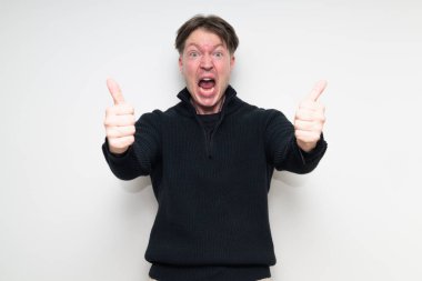 İskandinav orta yaşlı adam siyah süveter içinde beyaz stüdyo arka planına gülümsüyor ve baş parmak işareti yapıyor.