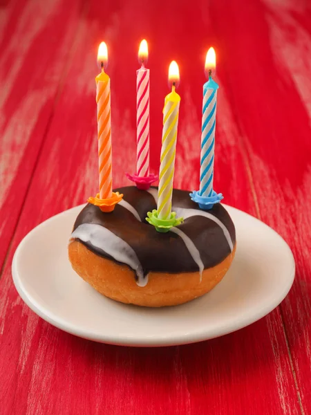 五颜六色的生日蜡烛与一个甜甜圈在红色木桌 — 图库照片