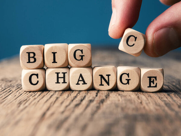 Small wooden dices with the word Change on an office table, hand puts the c on it