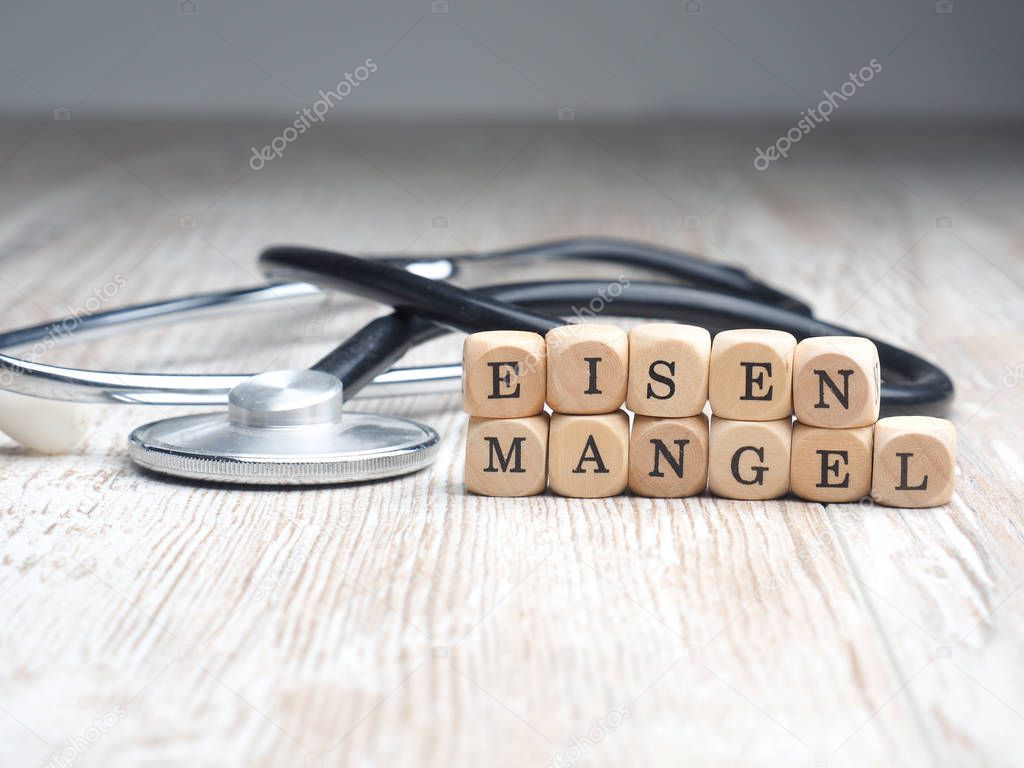 The German words iron deficiency on small wooden blocks with a stethoscope on a table, health care or medical concept