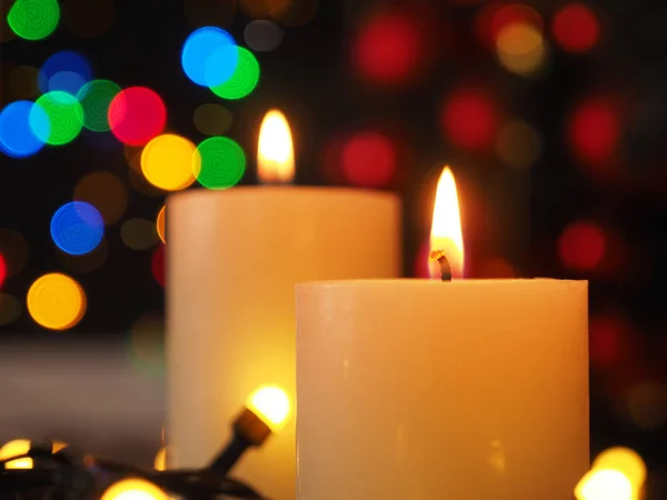 Zwei brennende Adventskerzen mit Weihnachtsbeleuchtung — Stockfoto