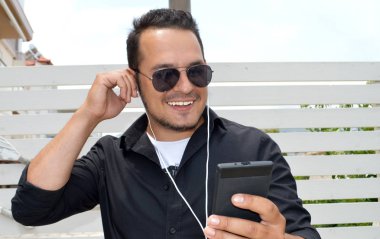 Bir akıllı telefon ile kulaklık kullanarak ve gülümseyen genç adam resmi