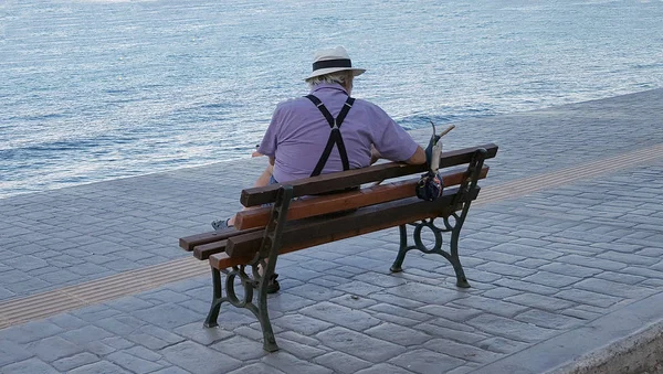 Old man sitting on the bench near the sea