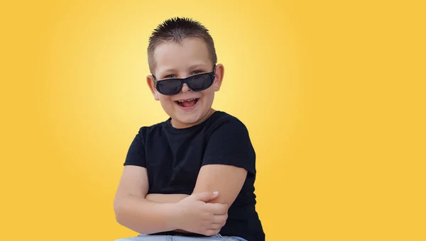 Mignon garçon a un grand sourire sur son visage regardant au-dessus de ses lunettes de soleil — Photo