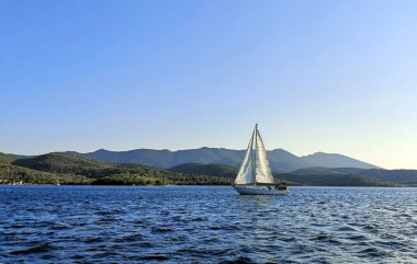Adanın yakınındaki denizde yelken açan yalnız bir yelkenli.