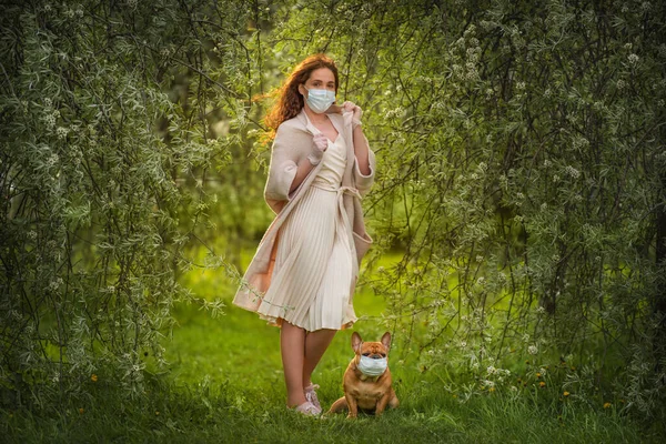 若い女性と彼女の犬フランスのブルドッグは医療マスクで公園を歩く 新常態 ロイヤリティフリーのストック画像