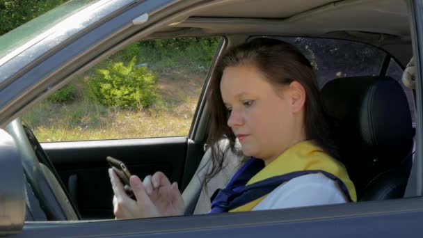 Mulher senta-se ao volante de um carro e usa um smartphone — Vídeo de Stock