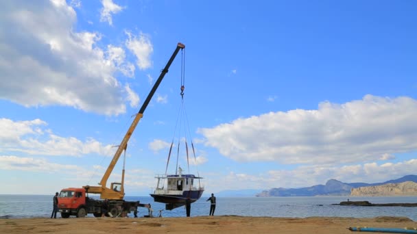 Кран поднимает голубую лодку из воды — стоковое видео