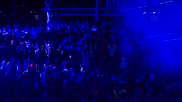 La gente balla ad un concerto alla luce di un riflettore blu — Video Stock