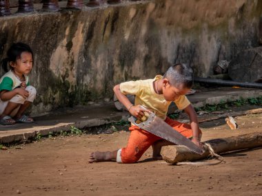 near pakbeng, laos - november 18, 2018: child with saw cuts clipart