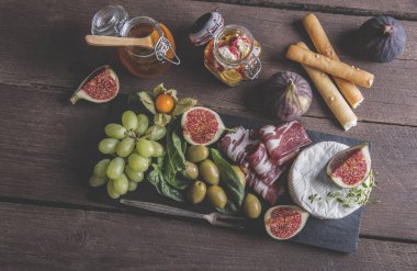 Prosciutto, camembert peyniri, incir, bal, üzüm, zeytin rustik ahşap arka plan üzerinde koyu hizmet gemide