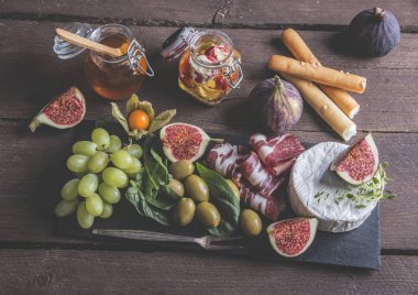 Prosciutto, camembert peyniri, incir, bal, üzüm, zeytin rustik ahşap arka plan üzerinde koyu hizmet gemide