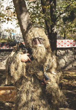 Kamufle keskin nişancı tüfeği tutar. Doğaya ghillie kamuflaj giysili asker.