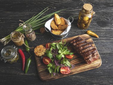 Biftek otlar, patates kızartması, baharatlar ile tahta üzerinde siyah bir yüzey üzerinde