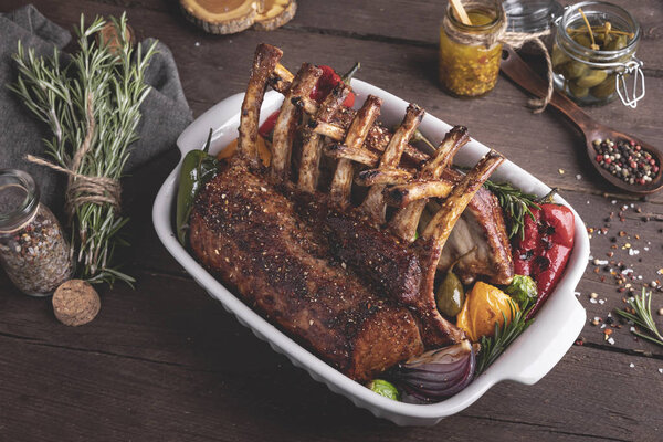 Grilled roasted rack of veal lamb chops with vegetables in ceramic baking dish.