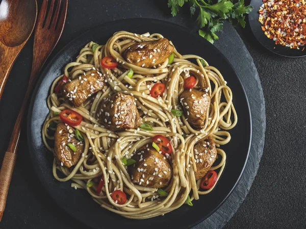 Asian noodles with chicken teriyaki , sesame, rustic stone background. Closeup. Chinese/Japanese noodles