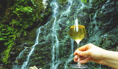 kadın el bir şelale ile arka plan kaya dağda beyaz şarap bir bardak tutan