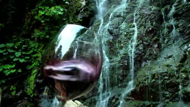 背景の岩と滝のガラスに赤ワインが飛び散る — ストック動画