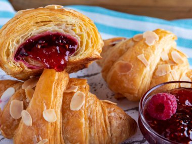 Lezzetli taze kruvasan, dilimlenmiş badem, ahududu reçeli kesimi, kapat.