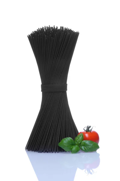 Svart spaghetti med baselblad och röd tomat på vit bakgrund — Stockfoto
