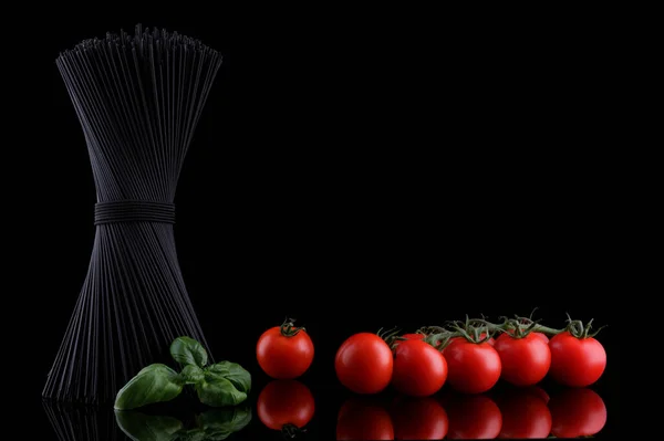 Svart spaghetti med baselblad och röd tomat på svart bakgrund — Stockfoto