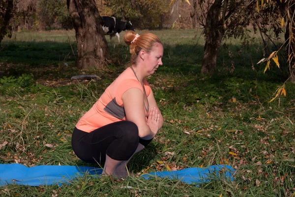 Middle-aged woman in an orange T-shirt practice yoga in nature