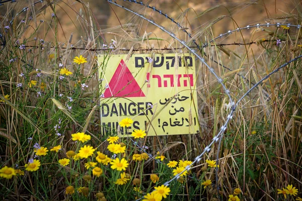 Minas de peligro - señal de advertencia amarilla junto a un campo minado, cerca de la frontera con Siria, en los Altos del Golán, Israel. — Foto de Stock