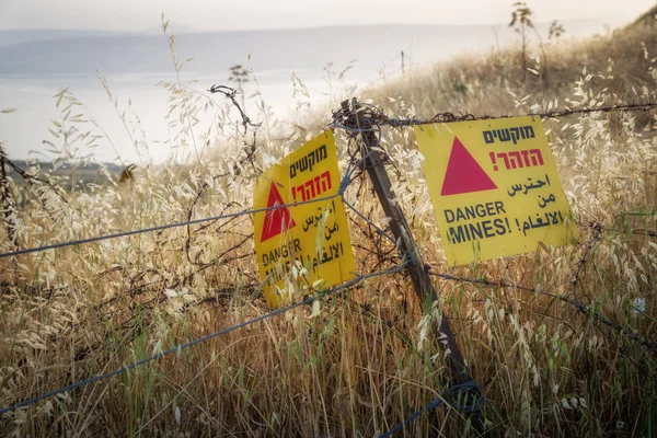 Minas de perigo - aviso amarelo ao lado de um campo de minas, perto da fronteira com a Síria, nas Colinas de Golã, Israel. — Fotografia de Stock