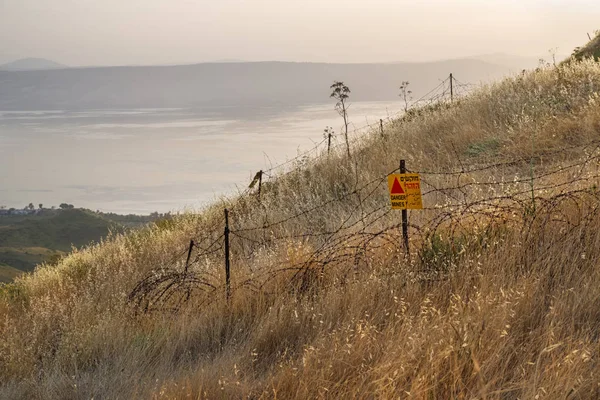 Niebezpieczne miny - żółty znak ostrzegawczy obok pola minowego, blisko granicy z Syrią, na Wzgórzach Golan, Izrael. — Zdjęcie stockowe