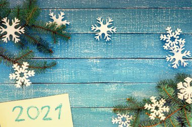 Mavi ahşap arka plandaki kar taneleri 2021 yılındaki beyaz arka plandaki Noel dalları 2021 yılını temsil ediyor.