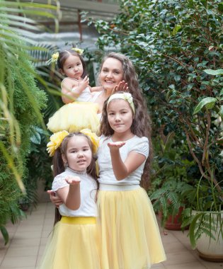 Mutlu kız kardeşleri ve annesi botanik bahçesinde yürüyüş. Sarı etek, büyük bir aile portresi kızlarda