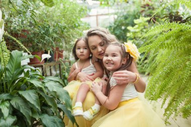 Mutlu kız kardeşleri ve annesi botanik bahçesinde yürüyüş. Sarı etek, büyük bir aile portresi kızlarda