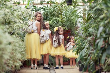 Mutlu kız kardeşleri ve annesi botanik bahçesinde yürüyüş. Sarı etek, büyük bir aile portresi kızlarda