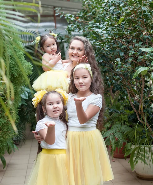 Mutlu kız kardeşleri ve annesi botanik bahçesinde yürüyüş. Sarı etek, büyük bir aile portresi kızlarda