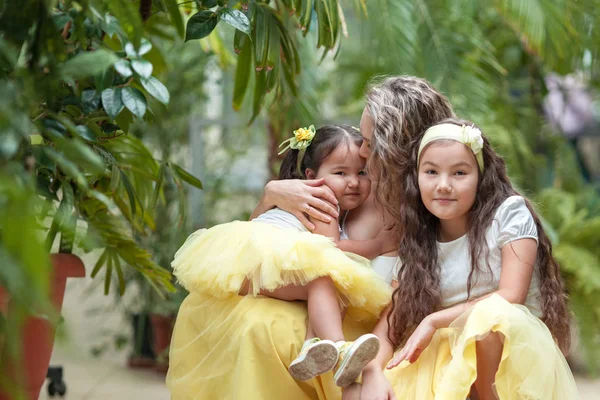 Mutlu kız kardeşleri ve annesi botanik bahçesinde yürüyüş. Sarı etek, büyük bir aile portresi kızlarda