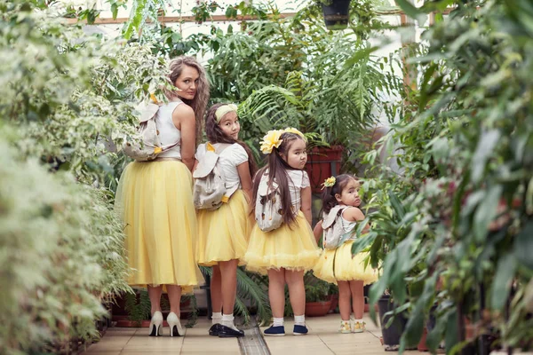 Mutlu kız kardeşleri ve annesi botanik bahçesinde yürüyüş. Sarı etek, büyük bir aile portresi kızlarda