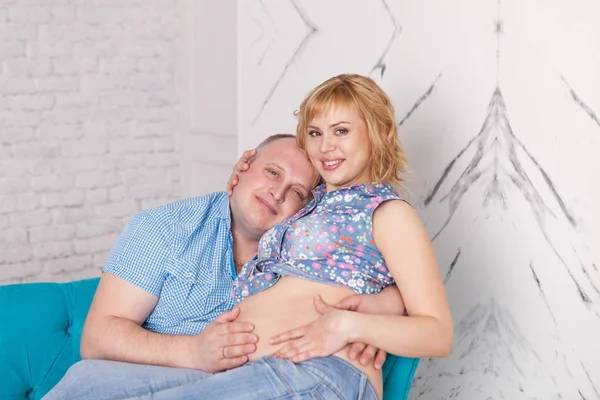 Evli çift portresi. Hamile kadın ve mutlu bir adam kanepede oturan ve sarılma, kapalı