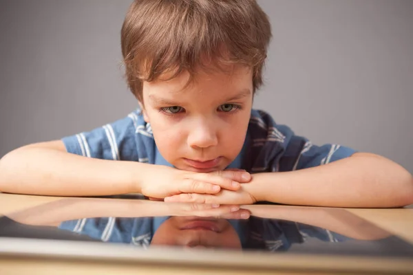 タブレット 灰色の背景に小さな男の子の肖像画で遊ぶ少年 — ストック写真