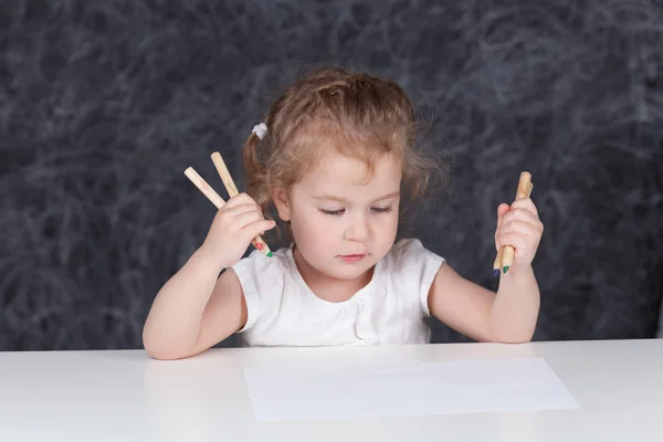 Little girl draws with pencils, portrait on background of school board, undoor