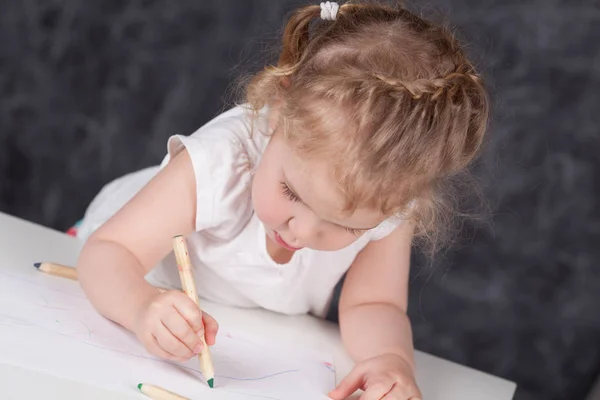 Little girl draws with pencils, portrait on background of school board, undoor