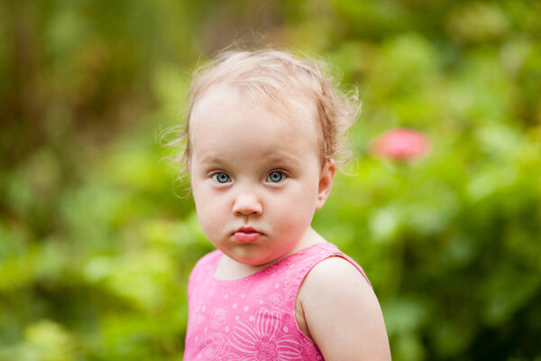 Портрет милой маленькой девочки в летнем саду на фоне цветов
