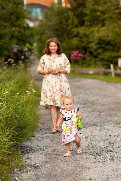夏の庭で幸せな陽気な母と娘の肖像画 家の近くの道路で赤ちゃんと歩いている女性は — ストック写真