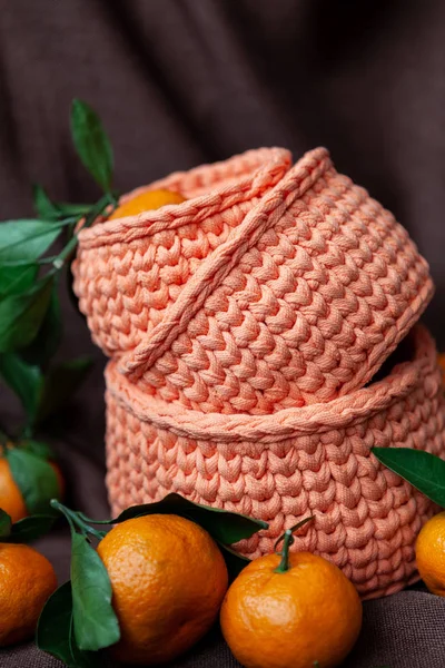 Orange knitted baskets with tangerines on brown background