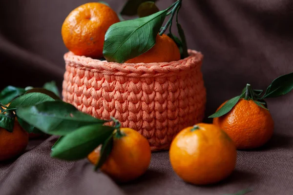 Orange knitted baskets with tangerines on brown background