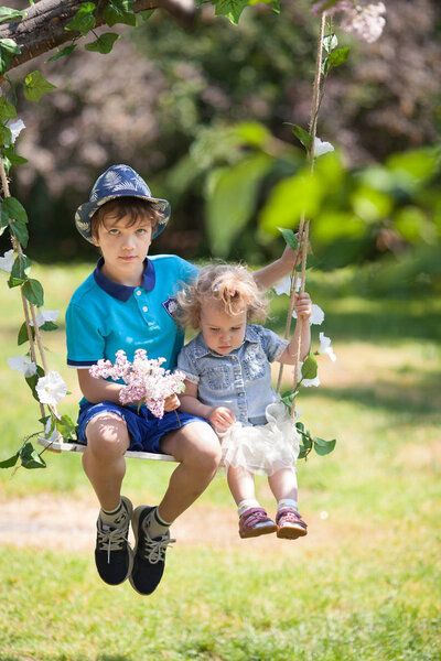 брат и сестра качаются на качелях в летнем парке, на открытом воздухе

