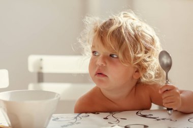 Küçük çocuk mutlu masada yiyor. Güzel kız kahvaltı parlak güneşli mutfak vardır..