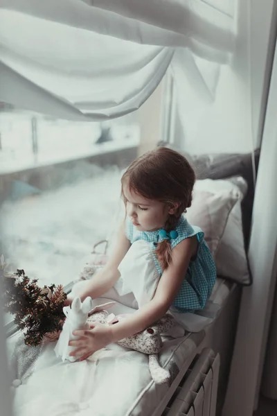 かわいい女の子の窓の近くに座っていると柔らかいおもちゃ Intdoor で遊ぶ — ストック写真