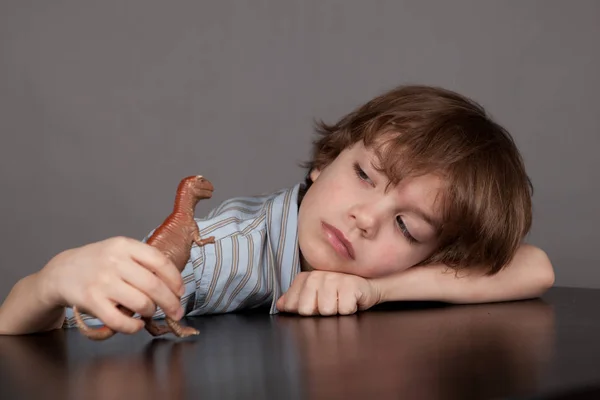 Denkender Schöner Junge Sitzt Schreibtisch Und Spielt Mit Dinosaurier — Stockfoto