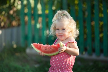 Mutlu küçük kız yaz bahçesinde karpuz yiyor, açık.